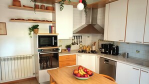 A kitchen with white cabinets, a microwave, oven, and a stove. There is a bowl of fruit on the table. - Spacious and cozy villa located between the sea and the volcano Etna! (Santa Maria La Stella)