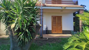 A two-story building with a balcony, a wooden door, and a large plant in the foreground. - Spacious and cozy villa located between the sea and the volcano Etna! (Santa Maria La Stella)
