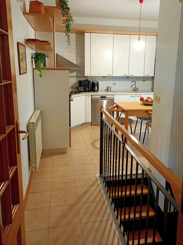 A kitchen with white cabinets, a wooden table, a black coffee maker, and a red hanging light.