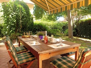 A wooden table set outdoors with chairs, a bottle, glasses, and a pitcher.