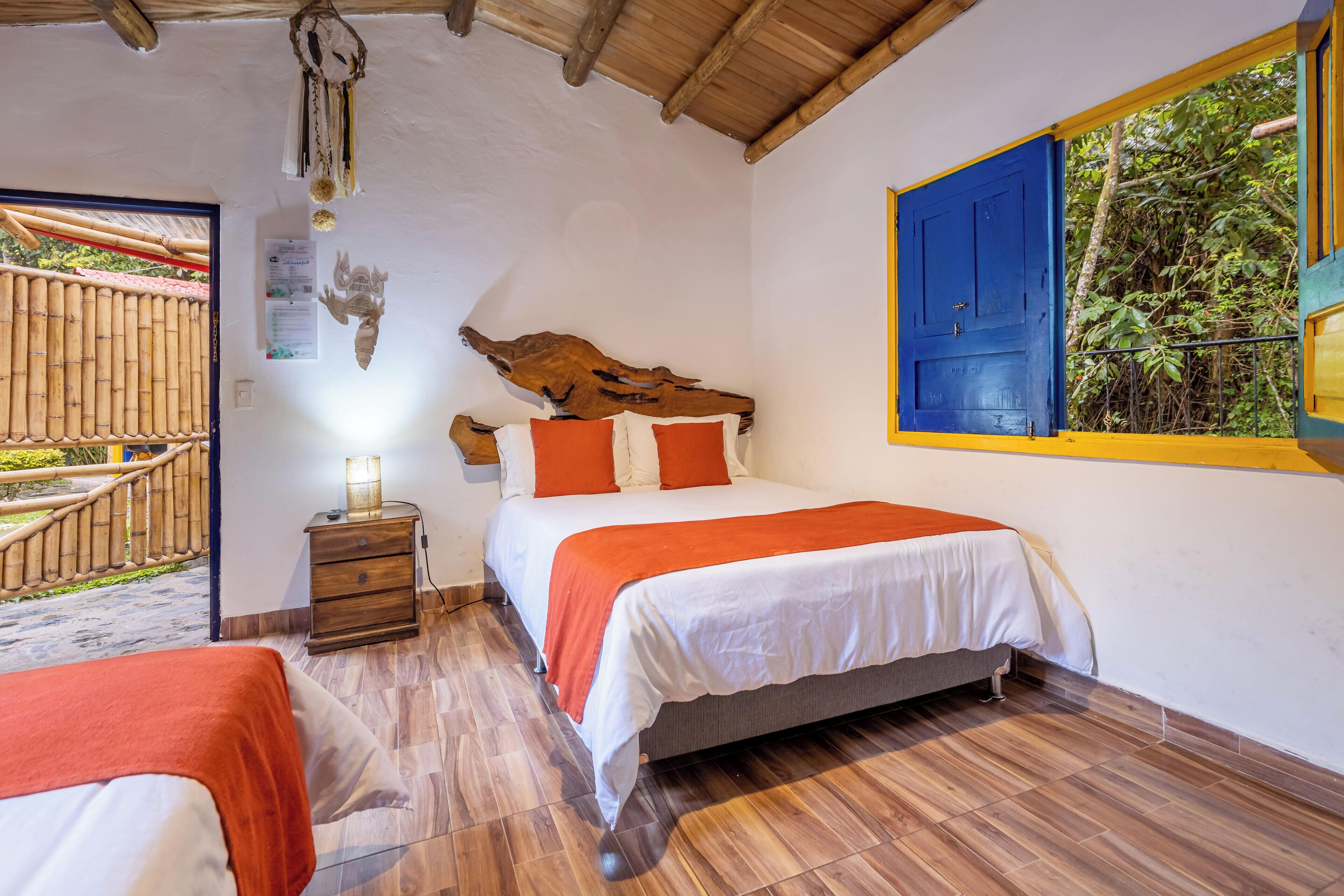 Un dormitorio con cama, mesita de noche, cabecera de madera, ventana con vistas a follaje y una valla de bambú en el exterior.