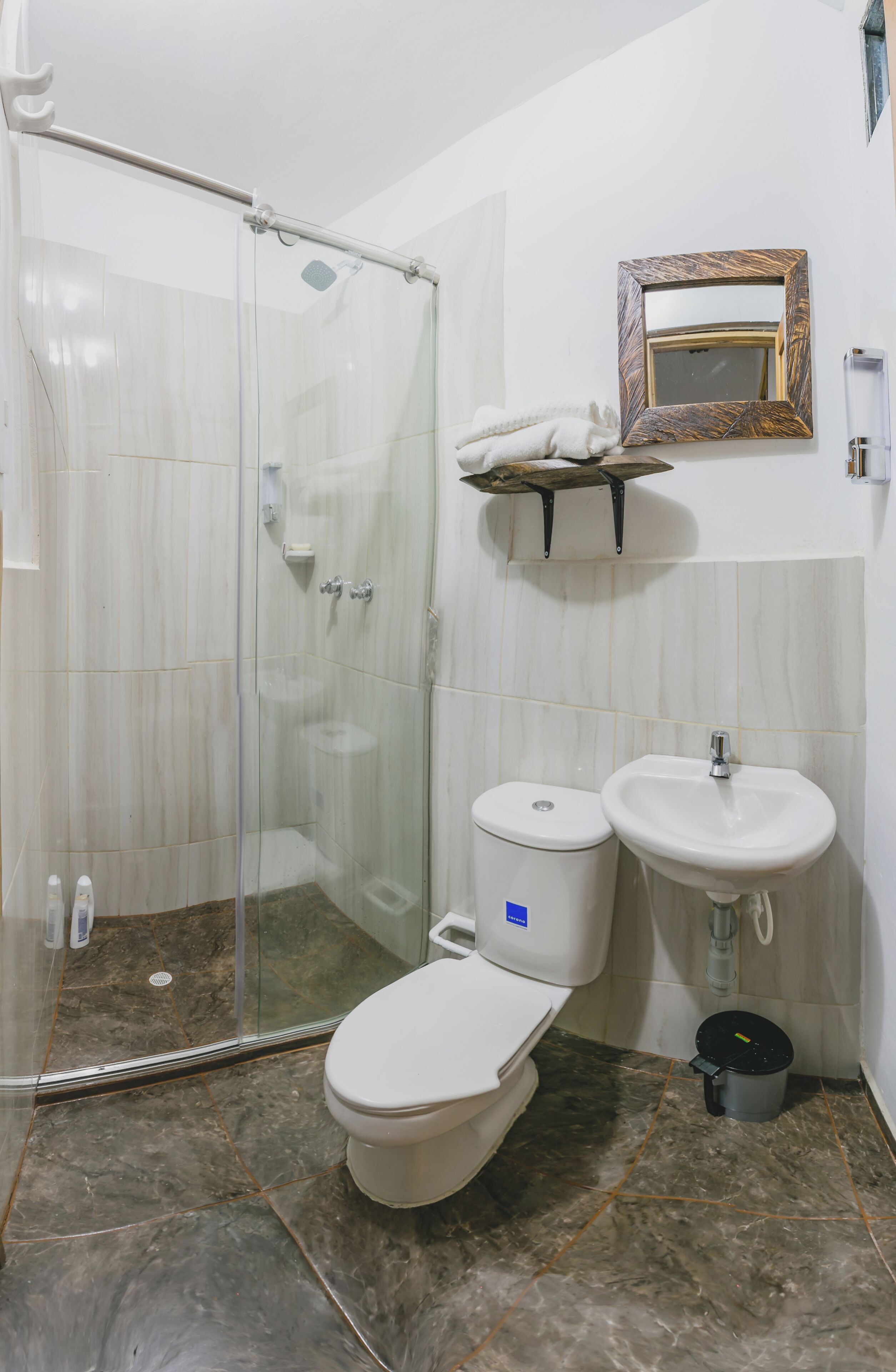 Un baño con ducha envuelta en vidrio, inodoro, lavabo y espejo con marco decorativo.