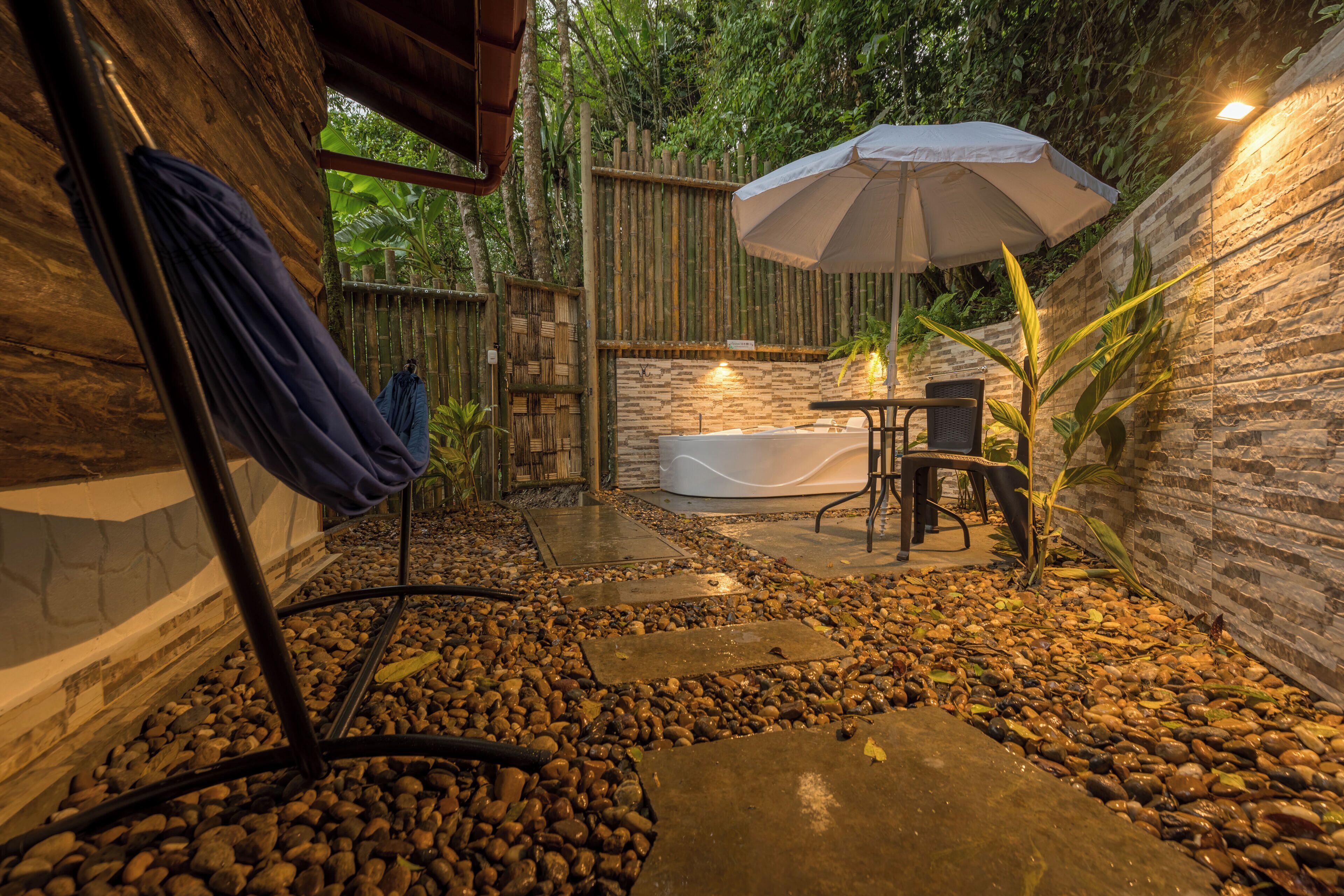 A private outdoor hot tub area with a stone wall, wooden fence, and an umbrella providing shade.