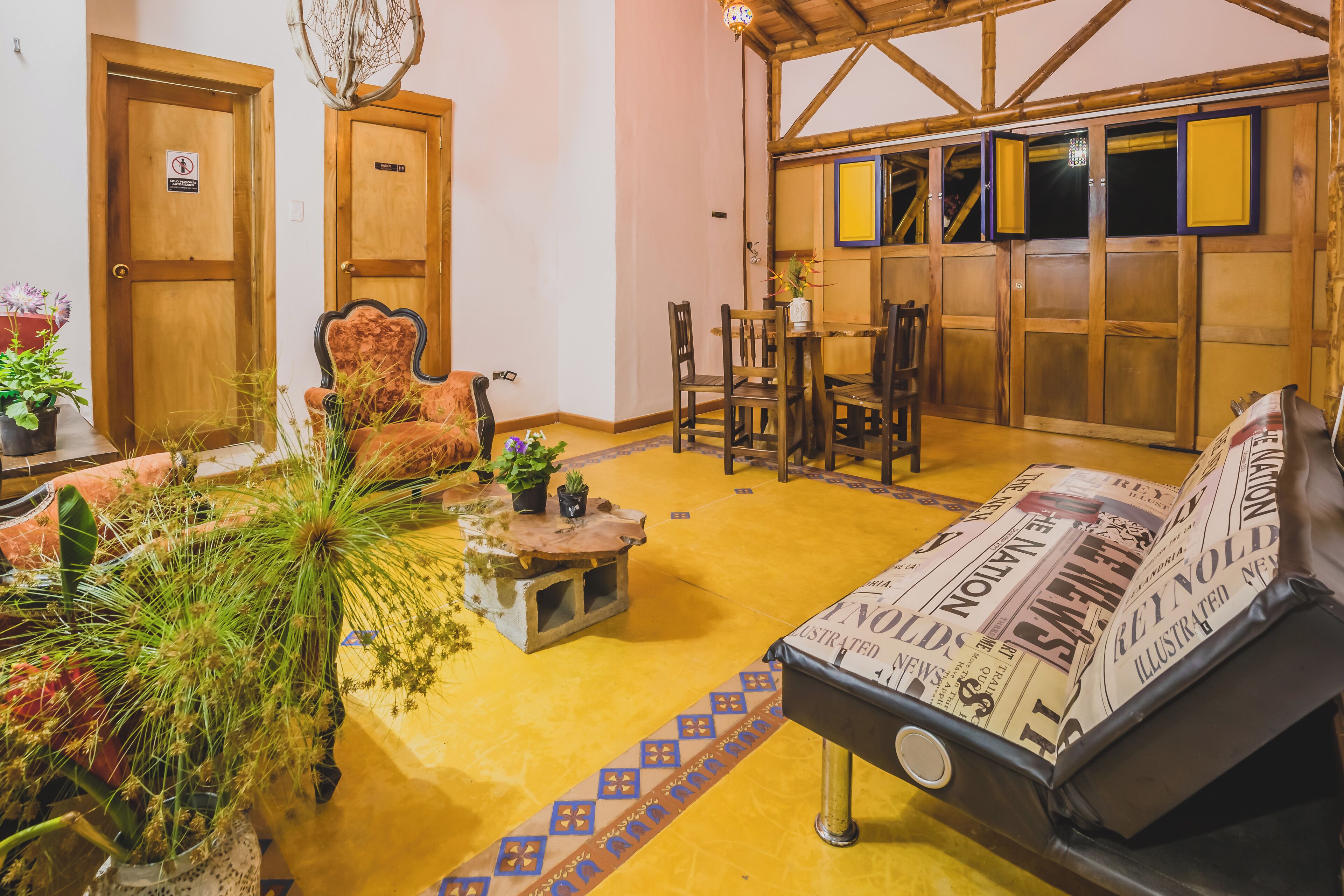 A cozy room with a wooden ceiling, a sofa with a newspaper cover, a dining table with chairs, and a door with a no-smoking sign.