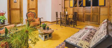 A cozy room with a wooden ceiling, a sofa with a newspaper cover, a dining table with chairs, and a door with a no-smoking sign.