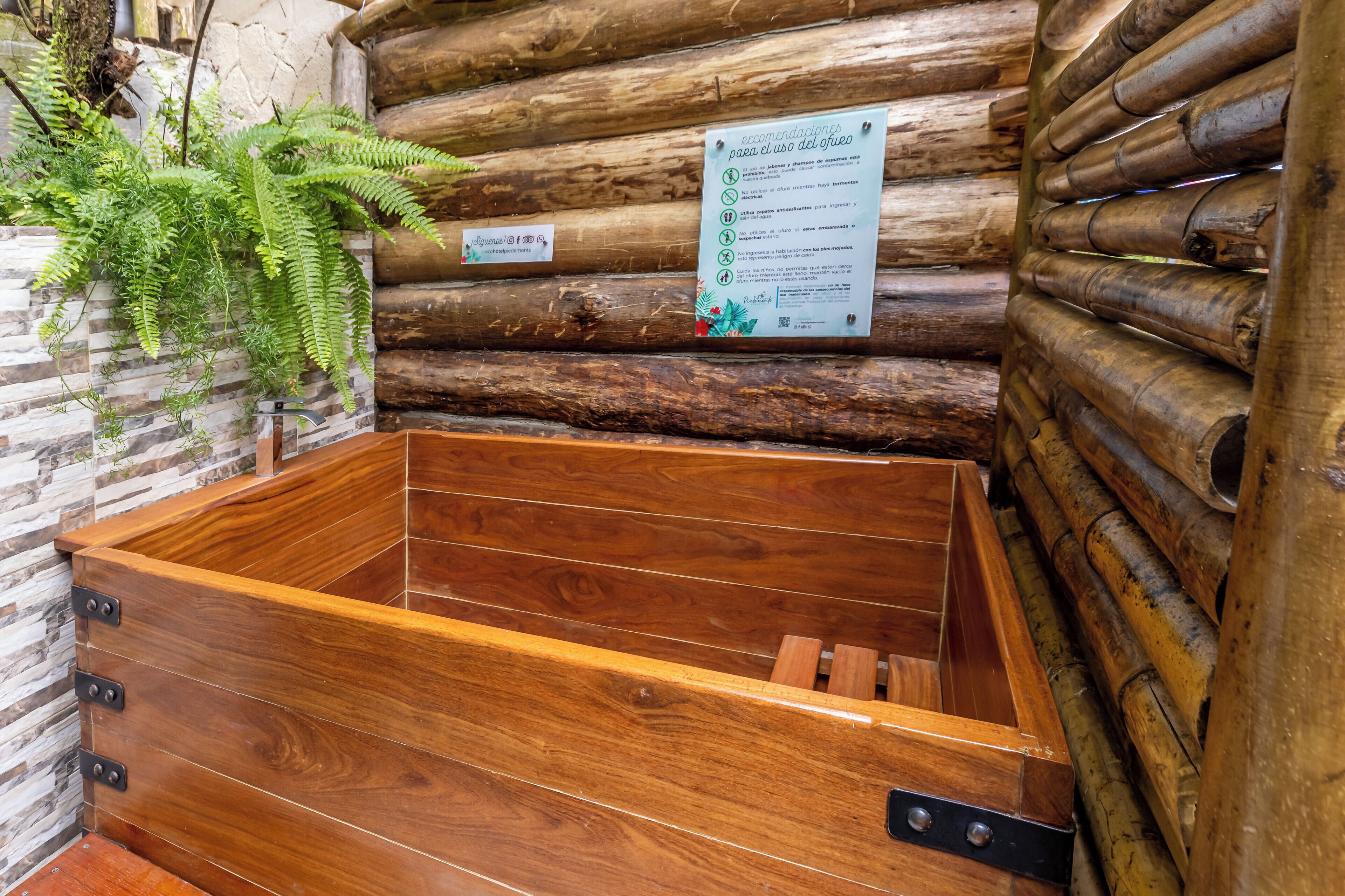 A wooden bathtub with a sign on the wall, a stone wall, and a wooden log structure.