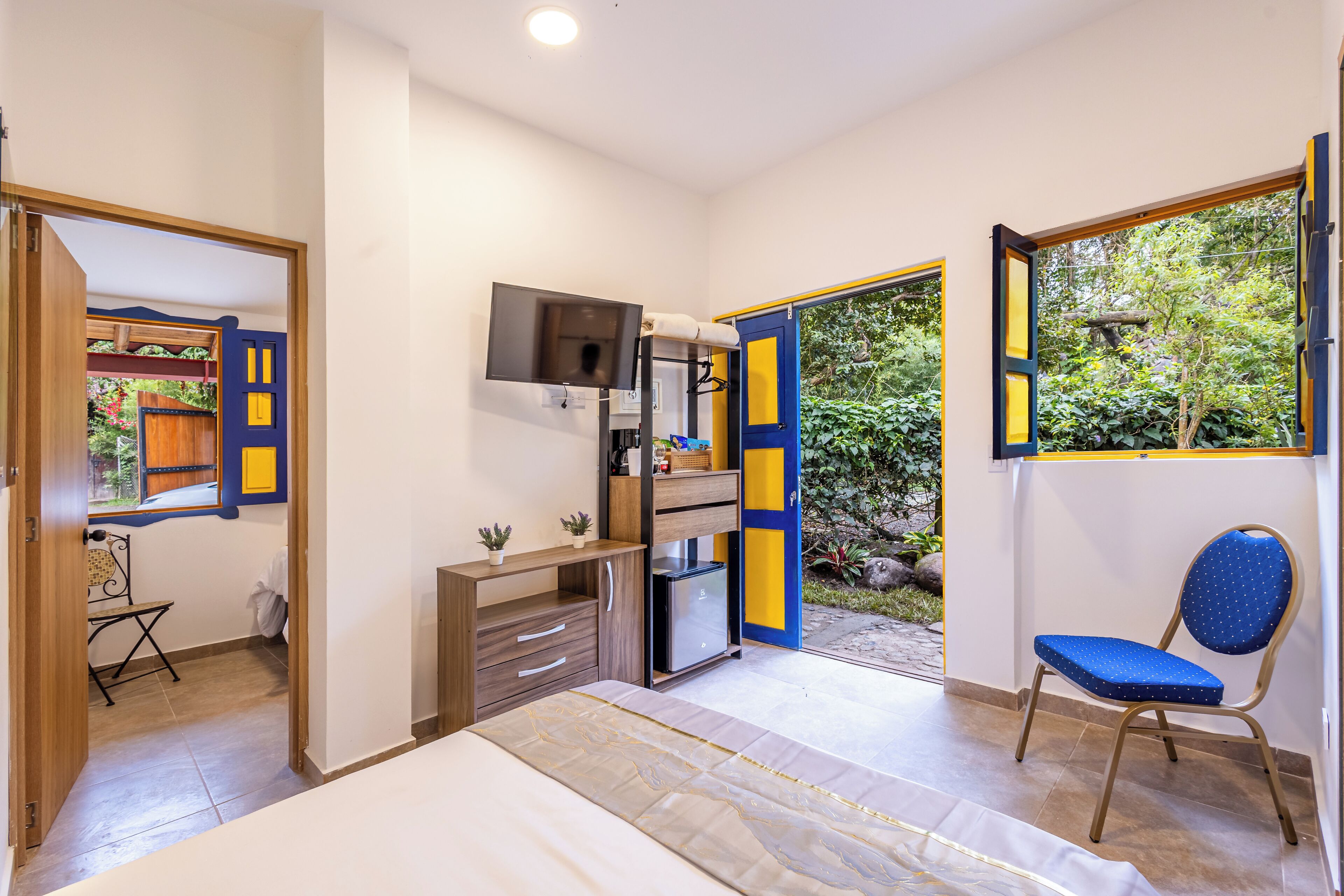 A bedroom with a bed, a desk, a chair, a TV, and a small fridge.