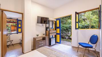 A bedroom with a bed, a desk, a chair, a TV, and a small fridge.