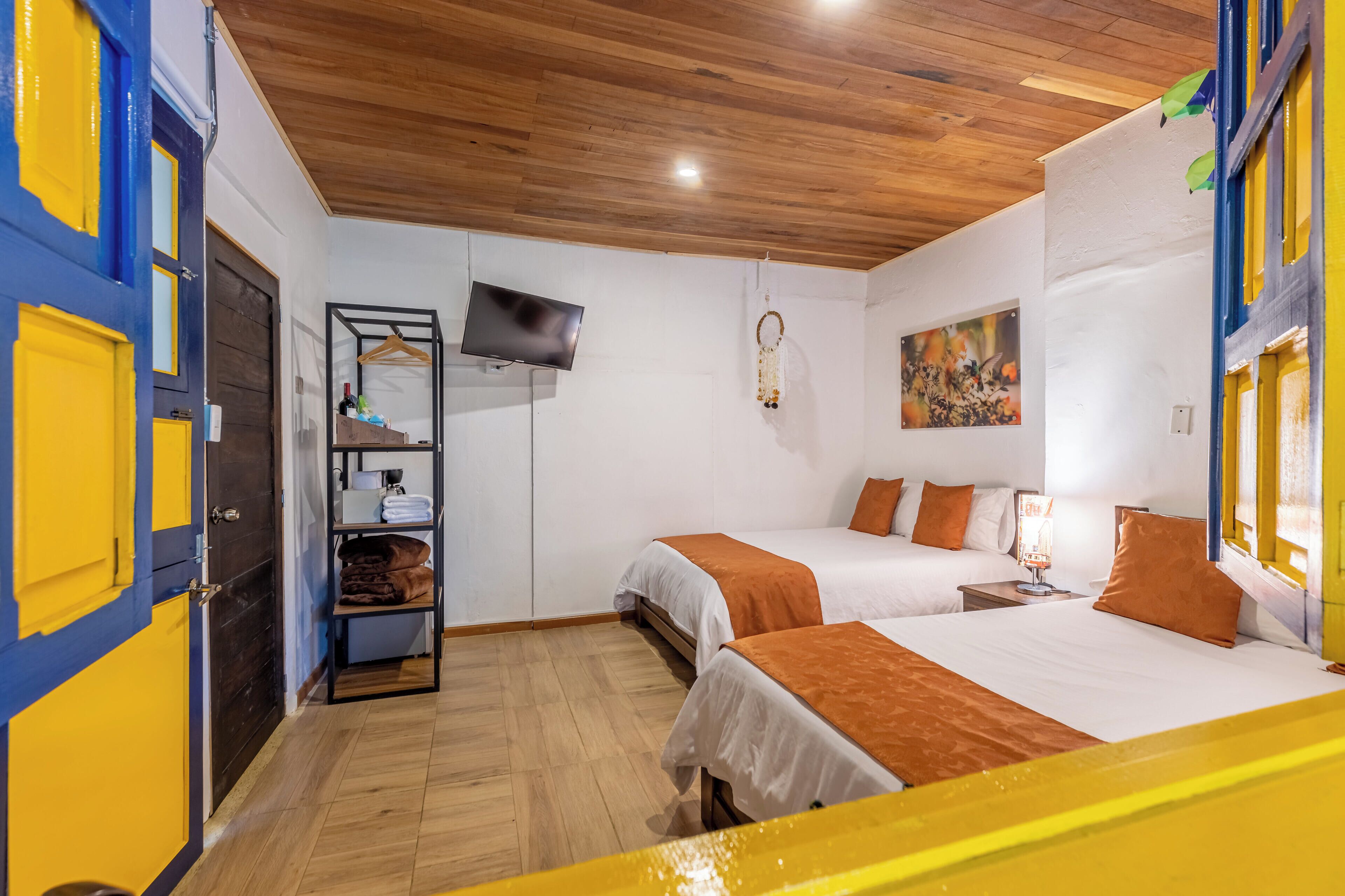 A hotel room with two beds, a TV, a shelf with toiletries, and a painting on the wall.