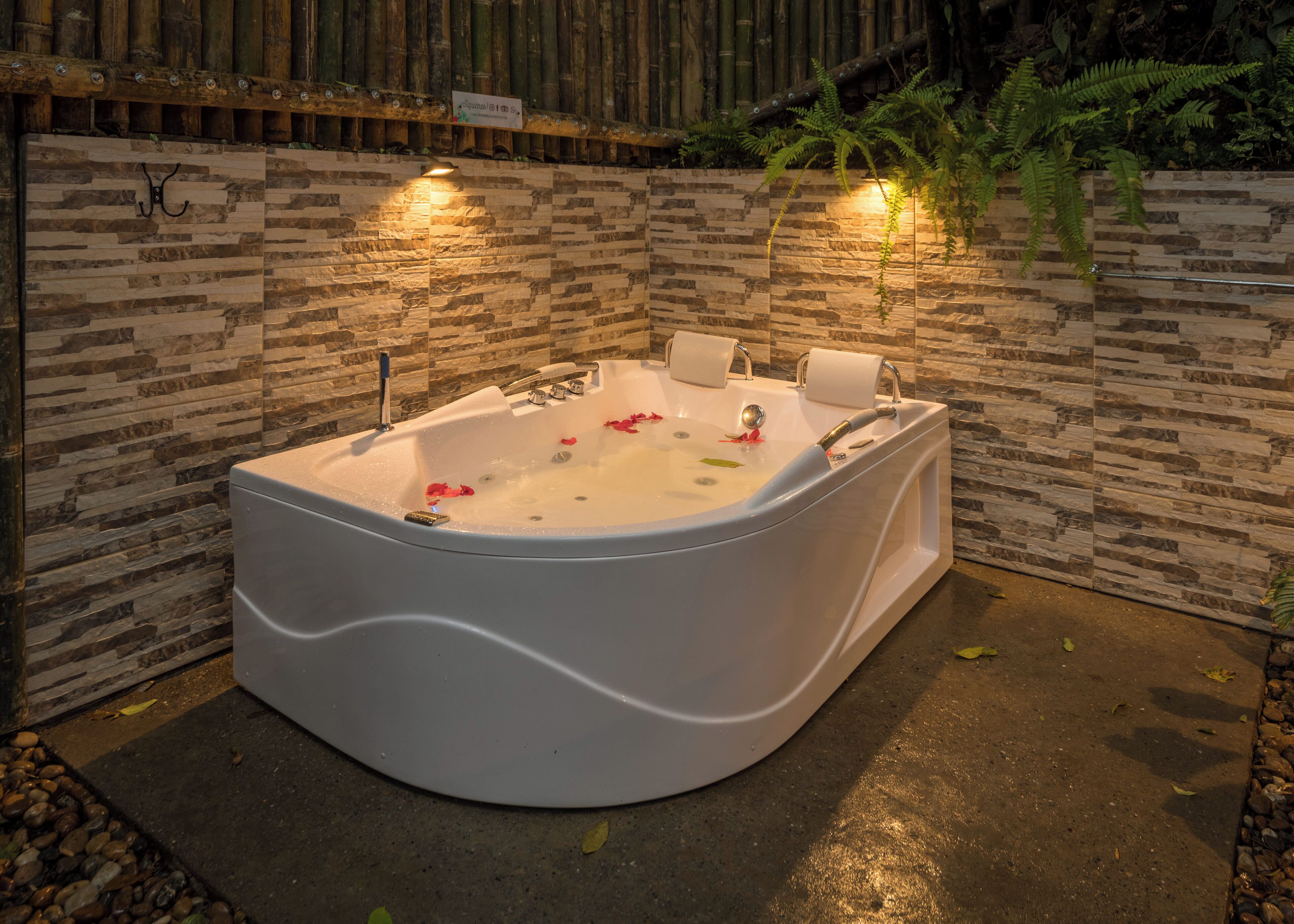 Een wellnessruimte met een groot, gebogen bubbelbad, omringd door stenen muren en bamboe decoratie.