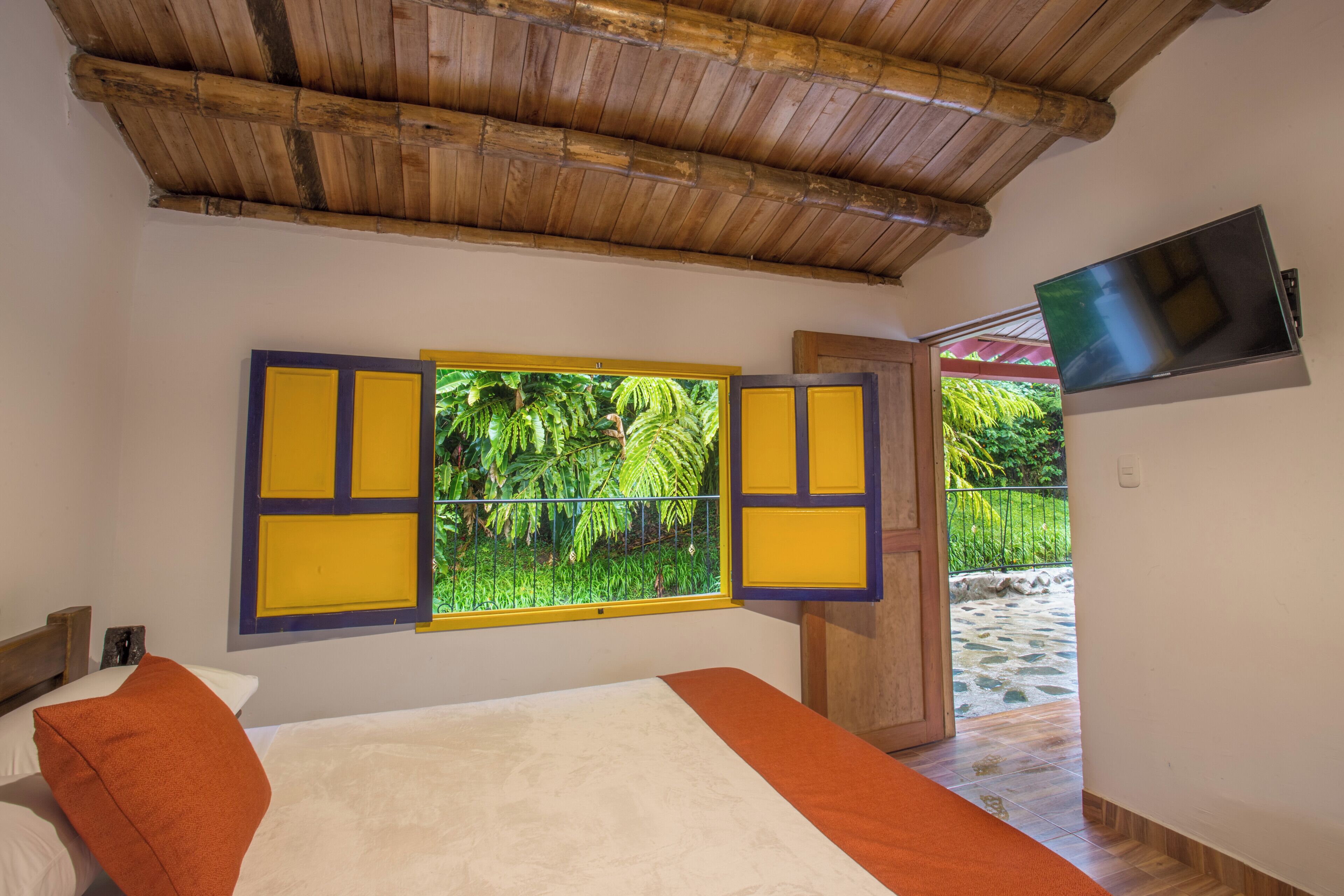 A room with a bed, a TV mounted on the wall, and a window with yellow shutters.