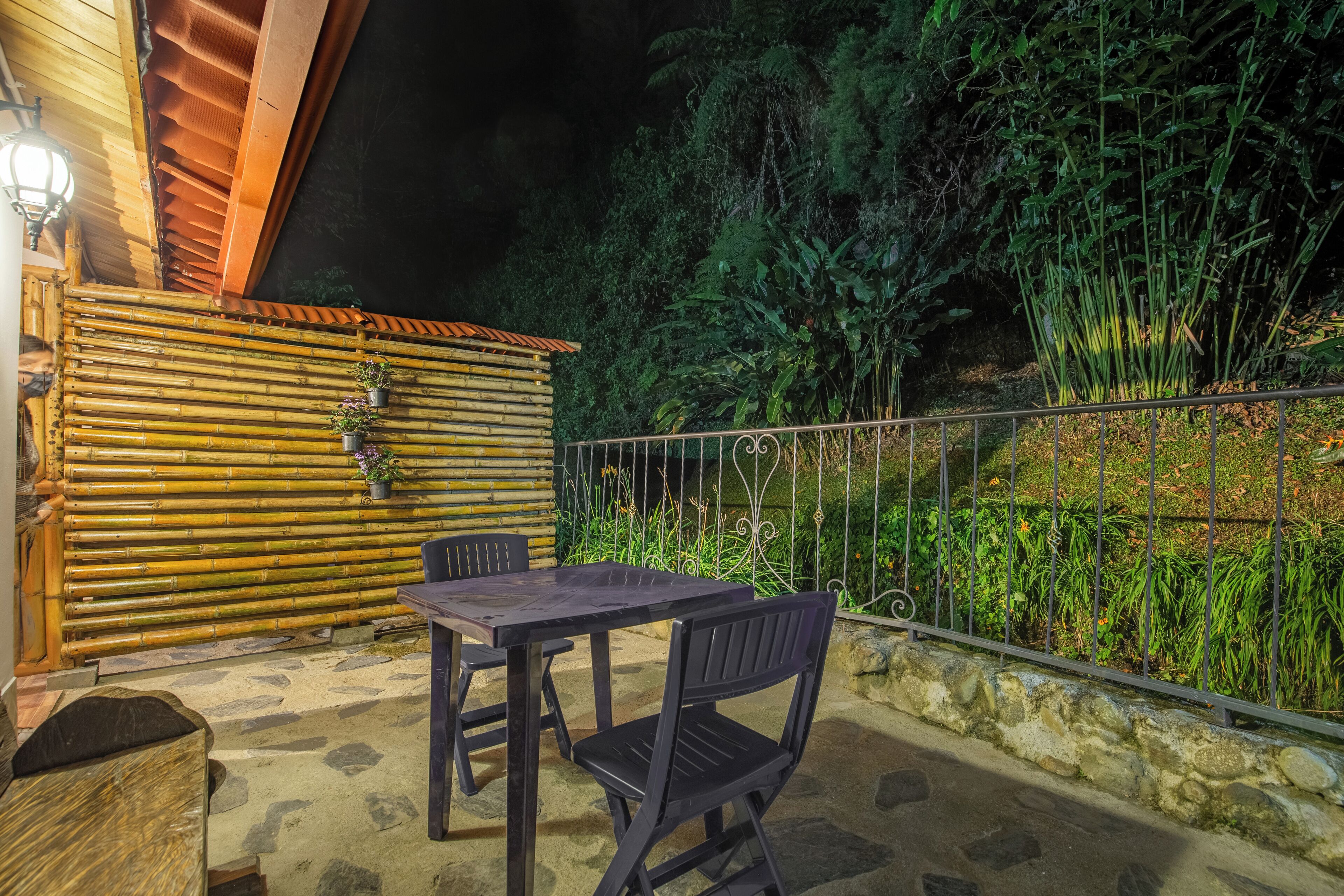 Un patio al aire libre con una mesa y sillas, rodeado de vallas de bambú y un muro de piedra.