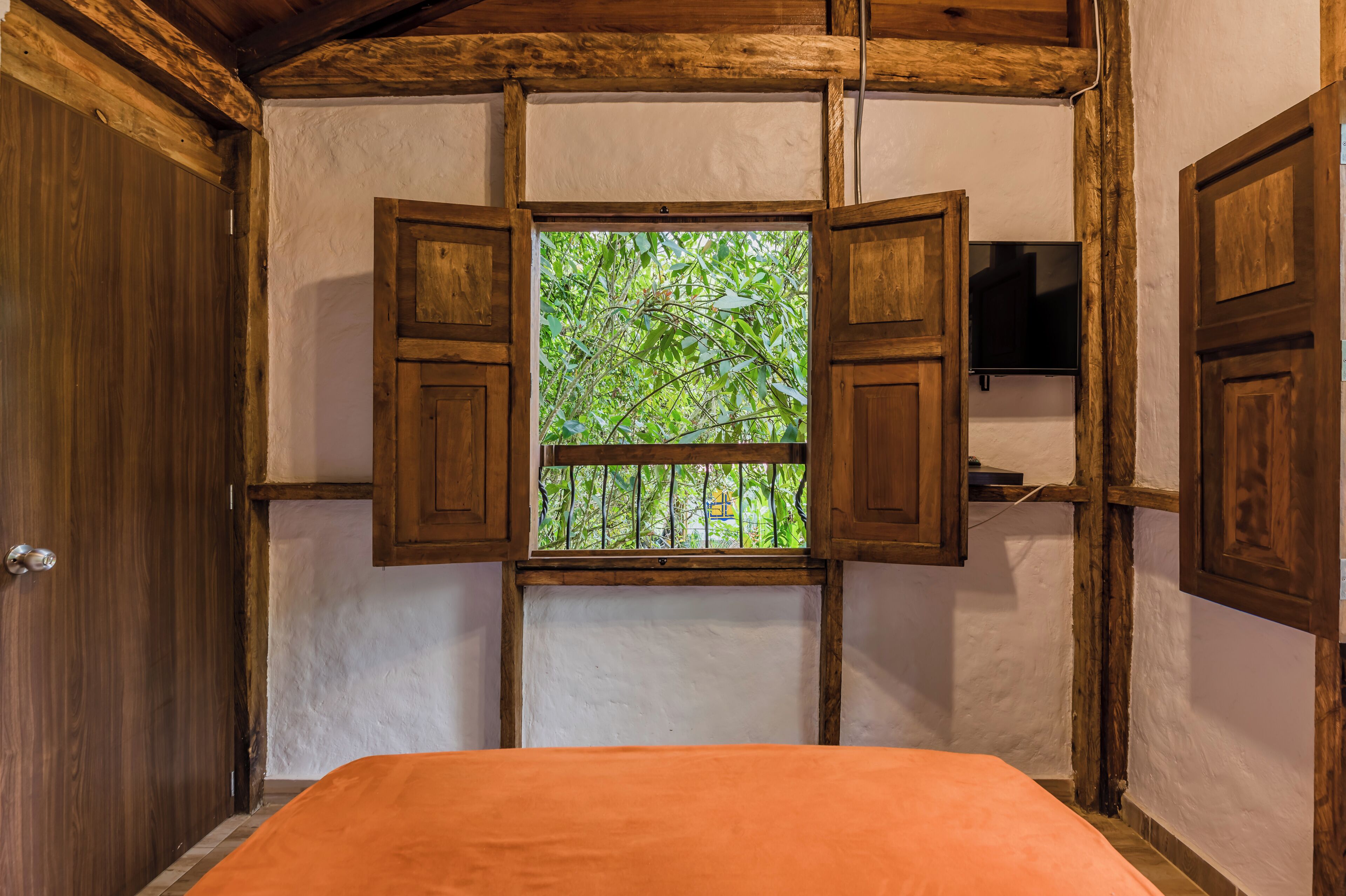Ein Schlafzimmer mit einem Bett, einem Fenster mit geöffneten Rollläden und einem an der Wand befestigten Fernseher.