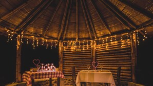 A cozy, rustic outdoor dining area with two tables set for a romantic meal, surrounded by wooden walls and string lights. - ECOHOTEL PIEDEMONTE (Salento)