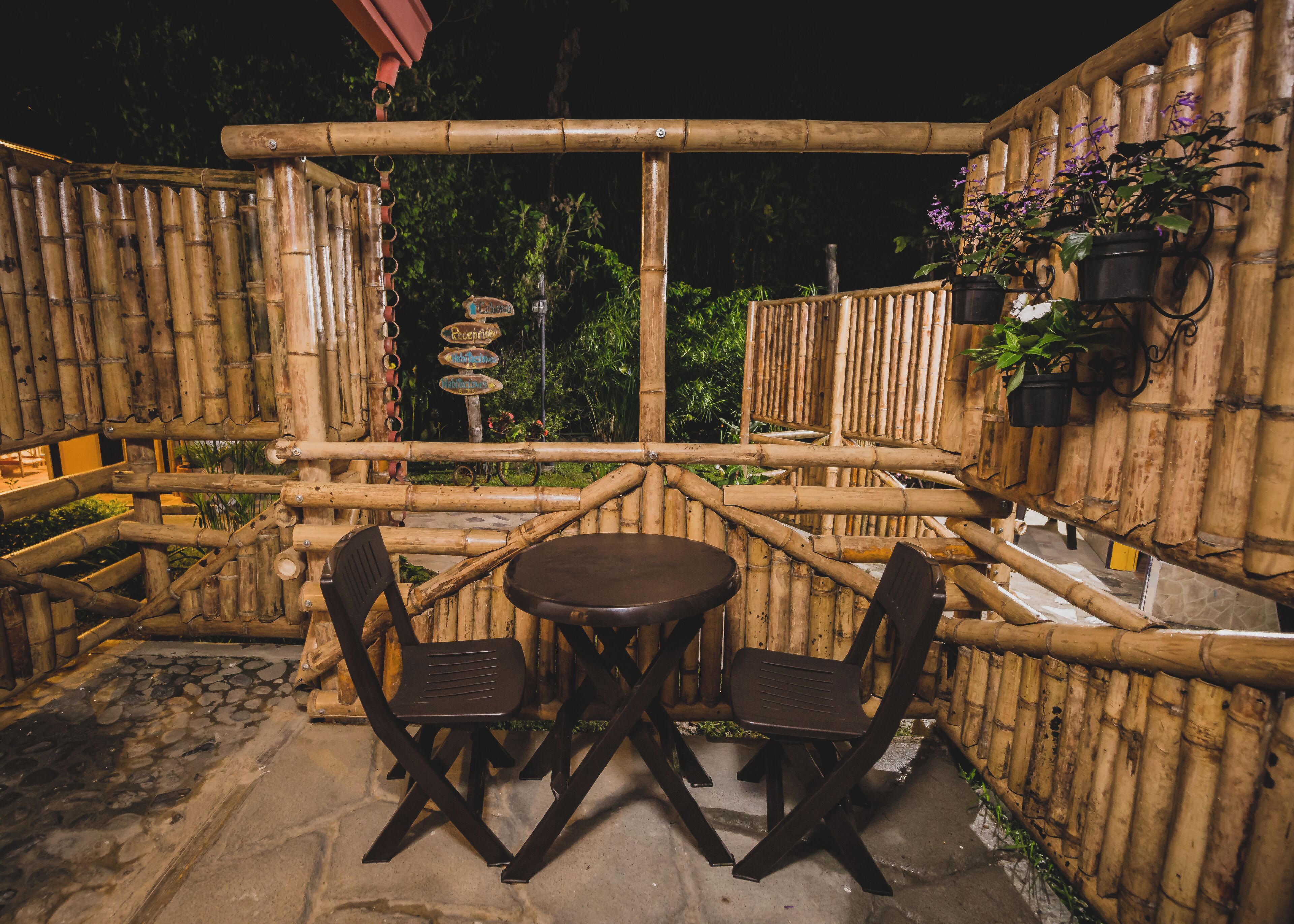 An outdoor seating area with bamboo walls, a stone floor, and a signpost with directional signs.