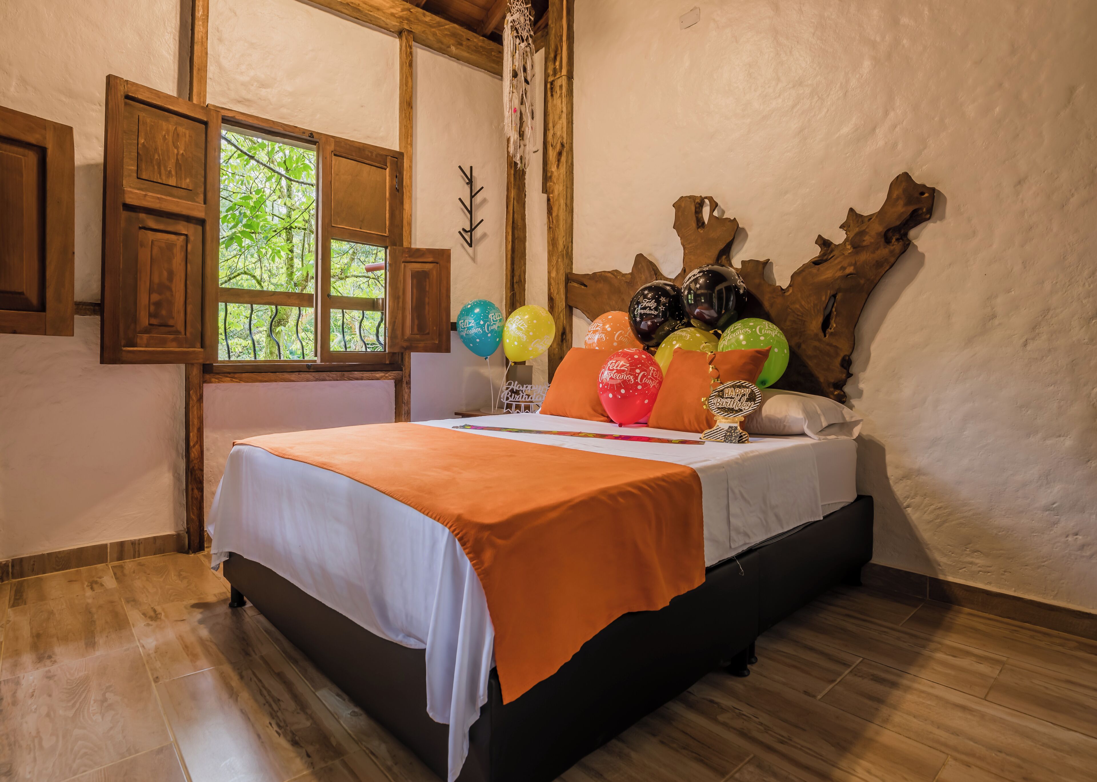 Une chambre avec un lit en bois, une fenêtre donnant sur un paysage verdoyant et un mur orné d’une sculpture en bois naturel.
