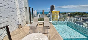 A rooftop pool area with a view of the city and ocean. - COBAR0142 - Edifício ZN Barra (Salvador)
