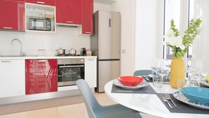 A modern kitchen with red cabinets, a built-in microwave, and a refrigerator. There is a dining table set with plates, glasses, and a vase of flowers. - Feel Naples New, Comfortable, bright and central 2 min from Metro! (Napoli)
