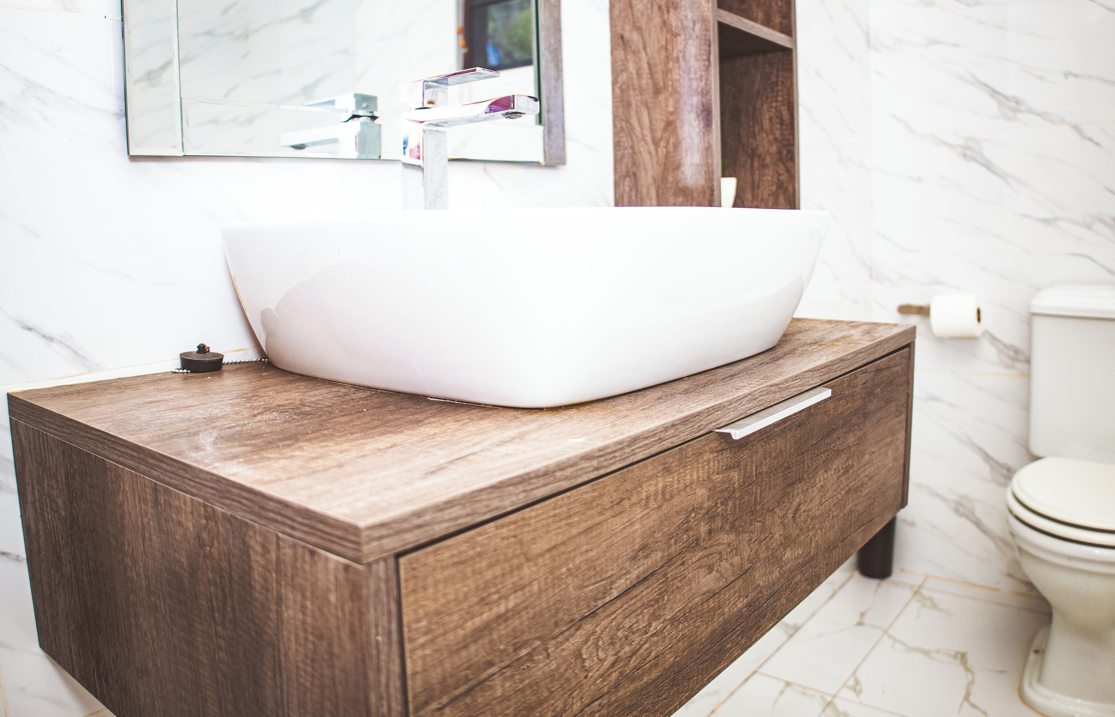 A bathroom with a wooden vanity, a white sink, and a marble floor.