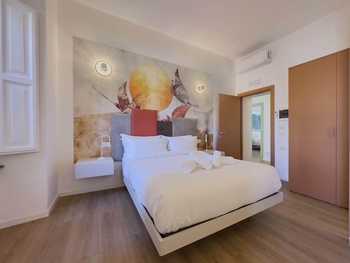 A modern bedroom with a large bed, a wall-mounted artwork, and a wooden floor.