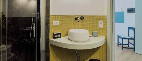 Une salle de bain moderne avec une douche à parois de verre, un lavabo blanc et un mur recouvert de carreaux jaunes.