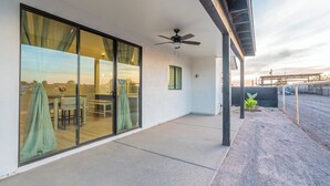 A modern patio area with a glass door leading to a dining space, a ceiling fan, and a view of a farm in the background.