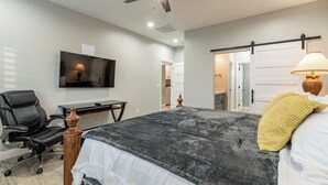 A bedroom with a bed, a desk, a chair, a TV mounted on the wall, and a ceiling fan.
