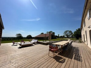 Una terraza de madera con mobiliario exterior, un muro de piedra y vistas al campo.