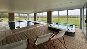 A spacious indoor pool area with a hot tub, wooden deck, and large windows offering a view of the outdoors. - Beautiful Villa With Indoor Pool (Sainte-Cecile)