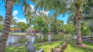 A serene outdoor area with a pond, palm trees, and two chairs facing the water.