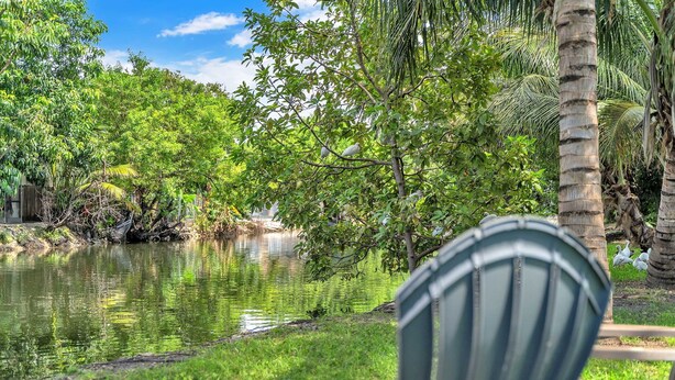 A serene outdoor setting with a pond, lush greenery, and a chair facing the water.
