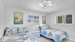 A bedroom with two beds, a ceiling fan, and artwork depicting sailboats.
