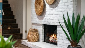 Una chimenea encendida, una escalera y cestas de mimbre sobre la repisa.