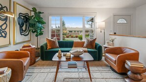 Una sala de estar con un sofá verde, dos sillones marrones, una mesa de centro y un ventanal con vistas a un edificio y árboles.