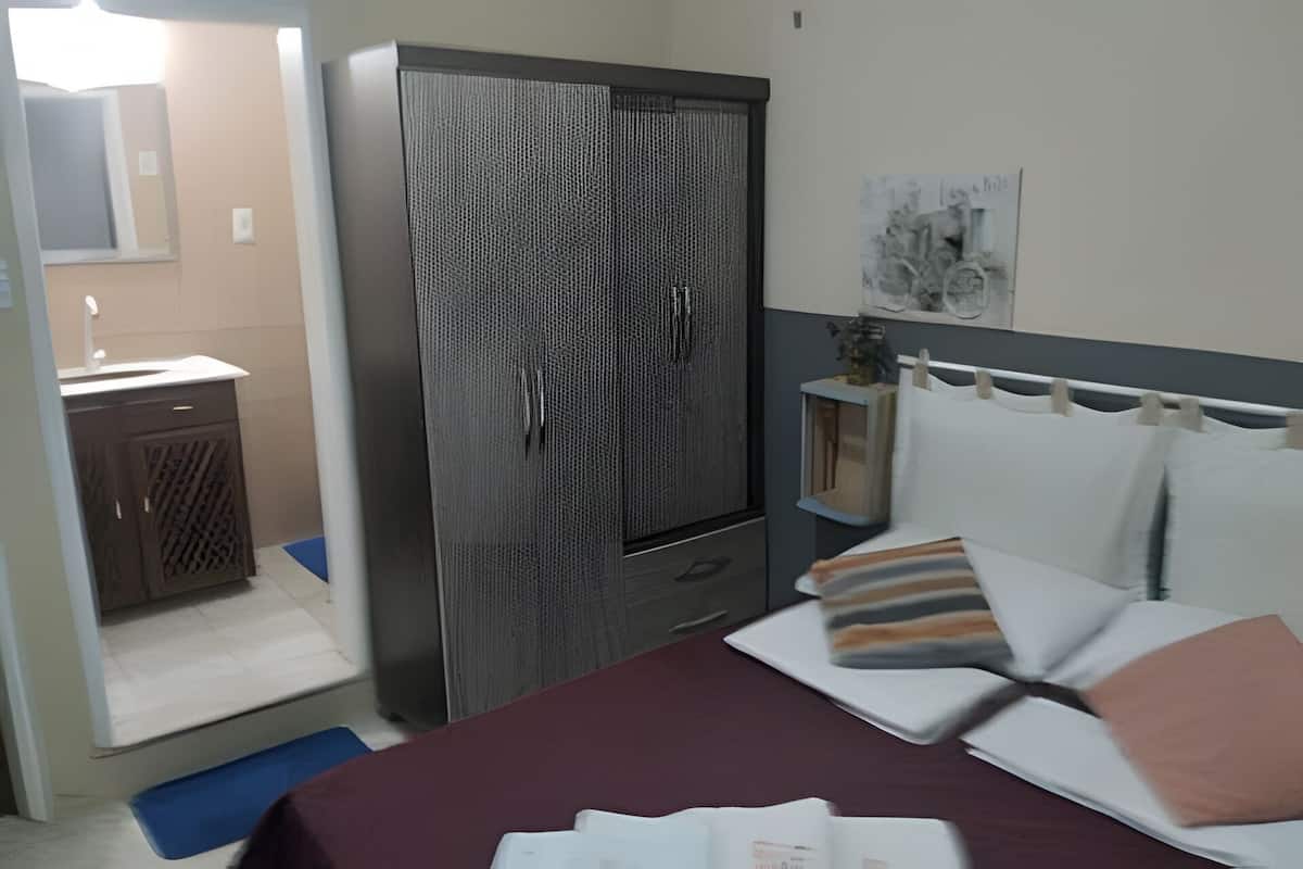 A bedroom with a bed, a wardrobe, a small desk, and a mirror.