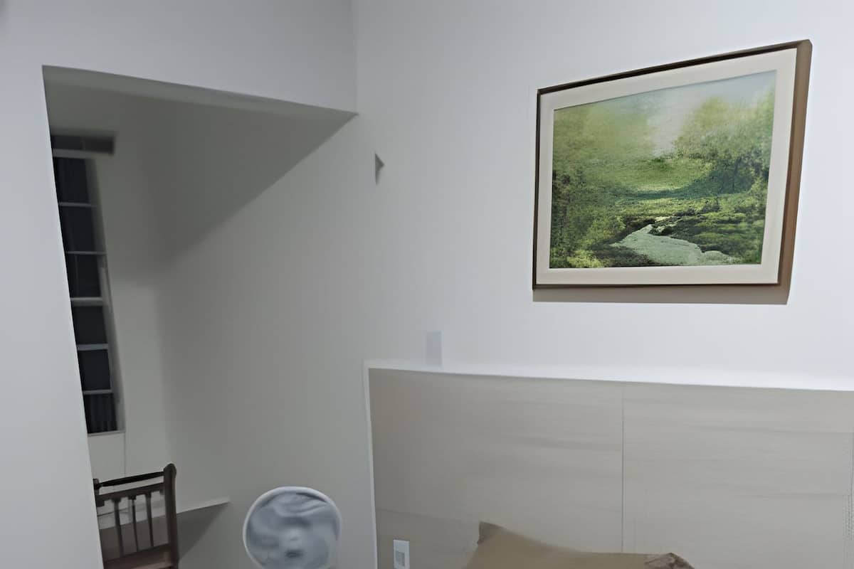 A bedroom with a bed, a bedside table, a chair, a small table with a mirror, and a painting on the wall.