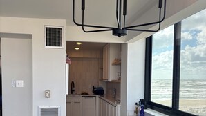 Et moderne køkken med hvide skabe, et spiseområde med et træbord og havudsigt gennem store vinduer.