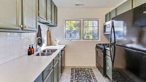 A kitchen with light green cabinets, a black refrigerator, a stove, and a window with a view of trees. - Nest & Nook • 2 Units, 2 Mins from BYU (Provo)