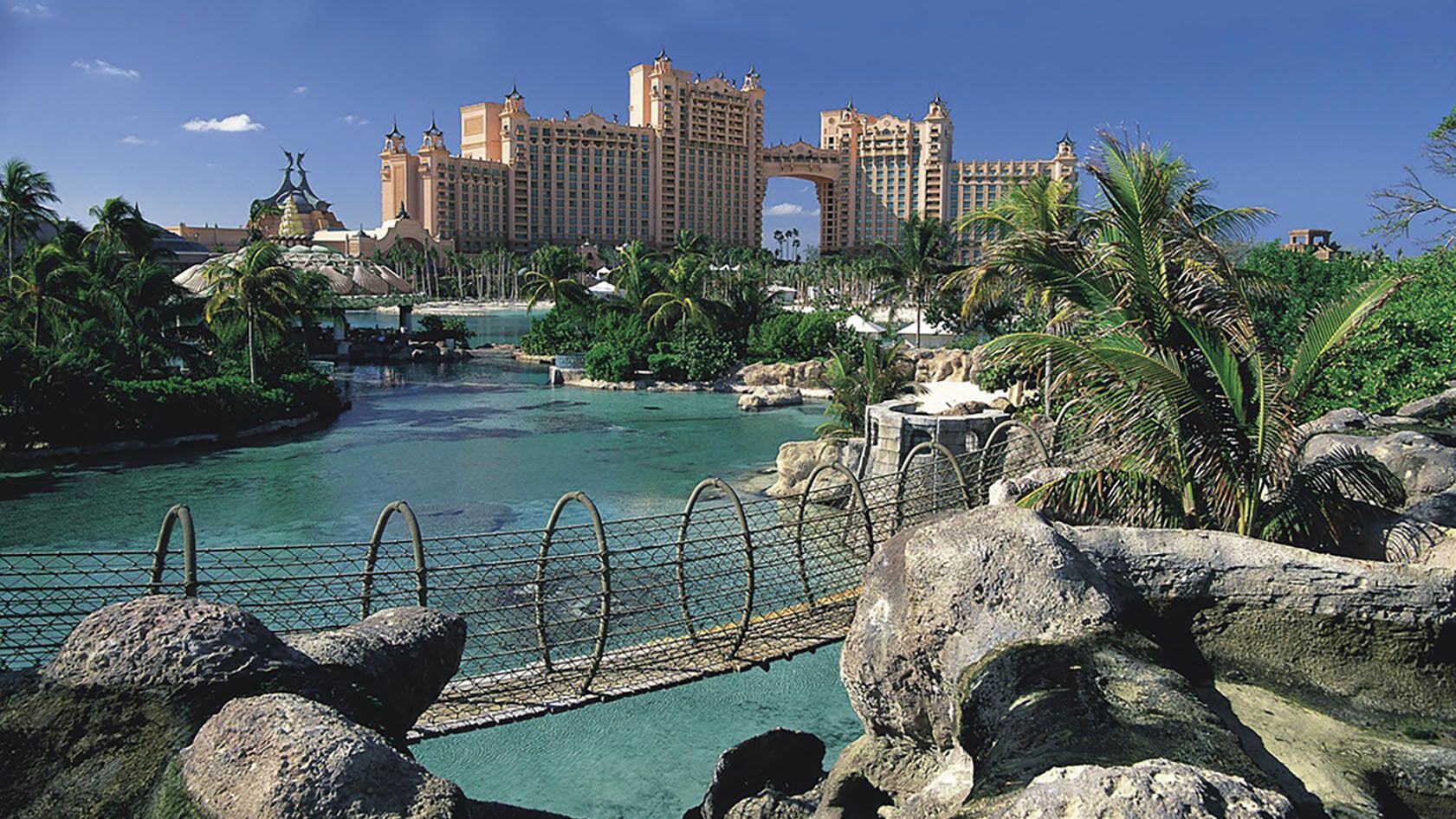 A resort with a large pool, palm trees, and a bridge.