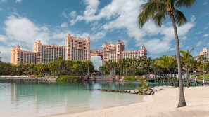 Un grand complexe hôtelier comprenant plusieurs immeubles de grande hauteur, une arche centrale, une plage bordée de palmiers et un pont enjambant une étendue d’eau.