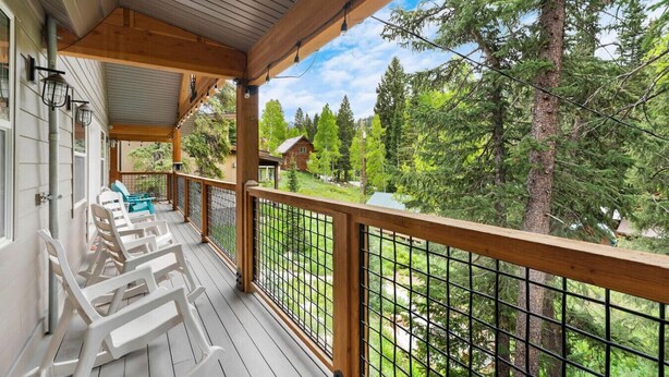 Una terraza de madera con sillas blancas y vista a un bosque.
