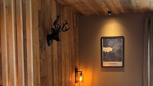 A bedroom with a wooden headboard, a mounted deer head, a framed map, and a bedside lamp. - Cosy studio in downtown Gérardmer (Gérardmer)