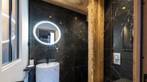 A modern bathroom with a marble sink, a round mirror with lights, and a wooden accent wall. - Cosy studio in downtown Gérardmer (Gérardmer)