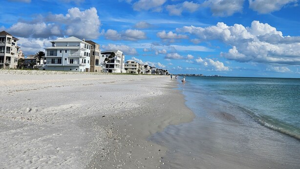 Ein Strand mit einer Reihe weißer Gebäude, wolkenlosem Himmel und ruhiger See.