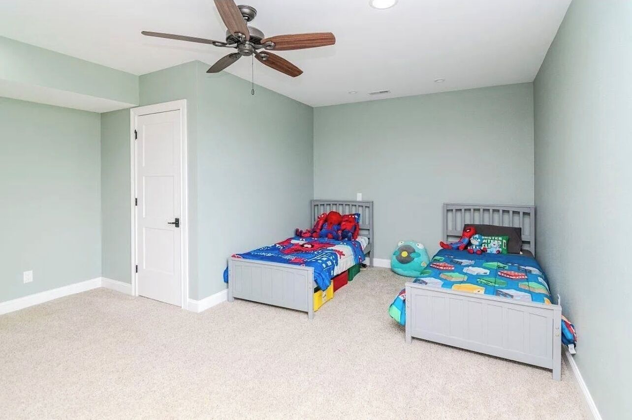 A bedroom with two single beds, a ceiling fan, and a door.