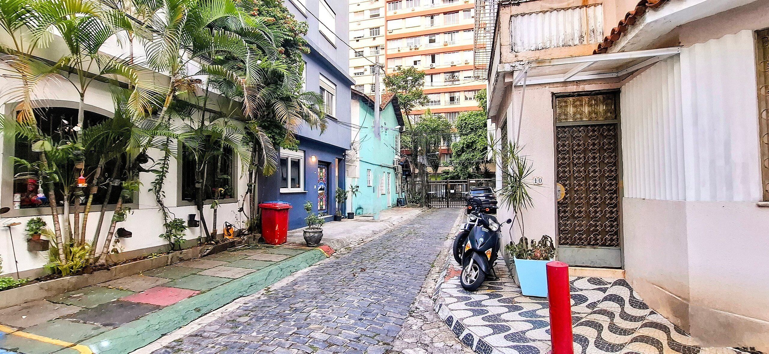 A narrow cobblestone street lined with residential buildings, some with balconies and potted plants.