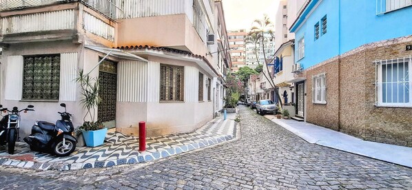 A narrow cobblestone street lined with buildings, some with balconies and others with barred windows.