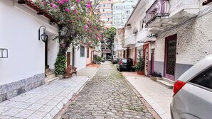 Una estrecha calle empedrada flanqueada por edificios, un coche aparcado y una escalera que lleva a una puerta.