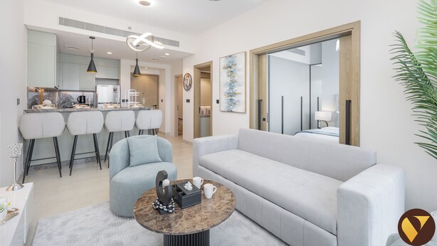 Un salon moderne avec un canapé gris, une table basse ronde et un coin repas, la cuisine étant visible au fond.