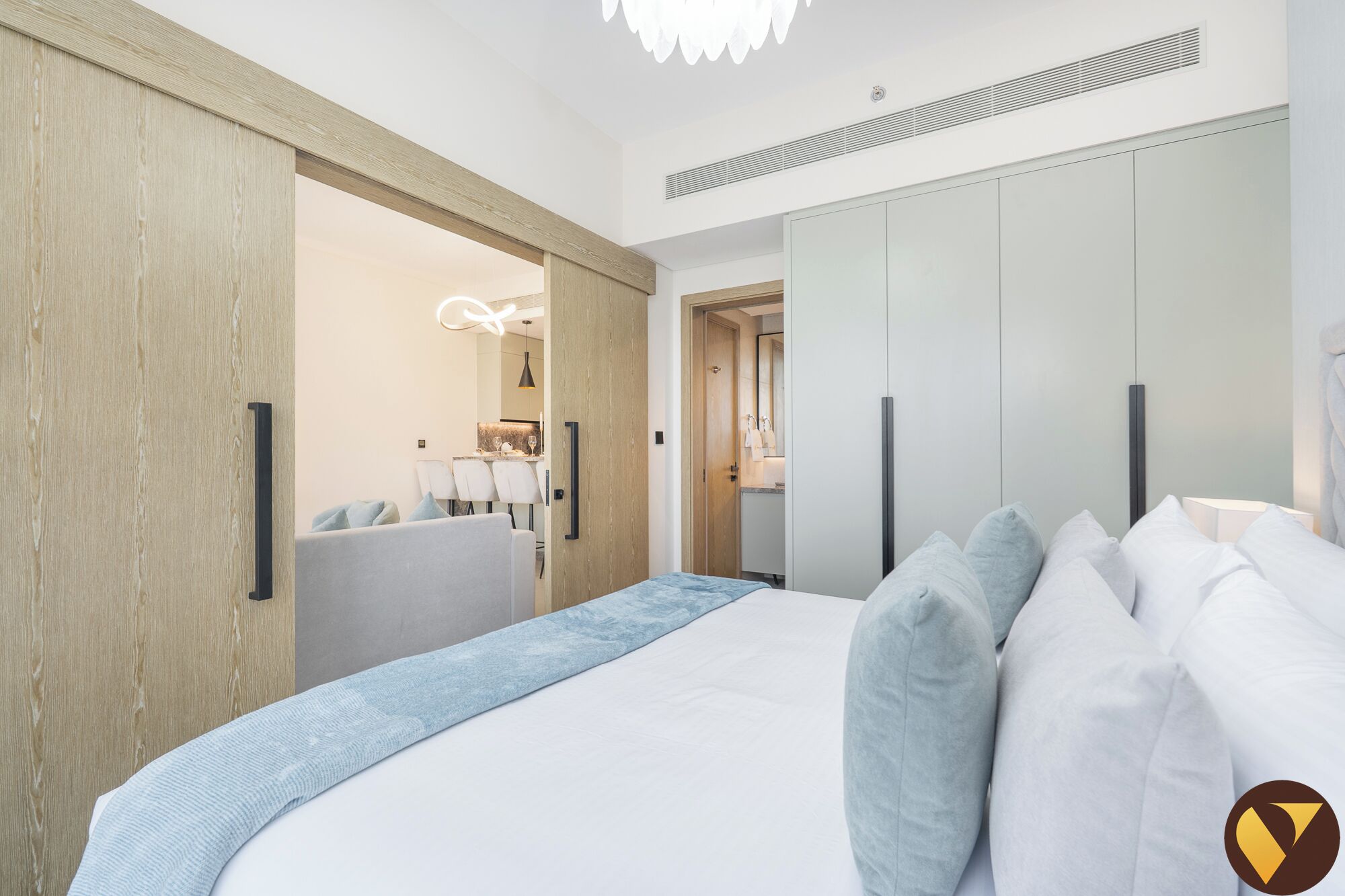 Ein modernes Schlafzimmer mit einem großen Bett, einem Holzschrank und einem Essbereich, der durch eine offene Tür sichtbar ist.
